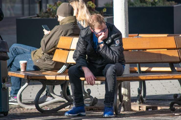 ragazzo seduto su una panchina con una mano sopra la bocca