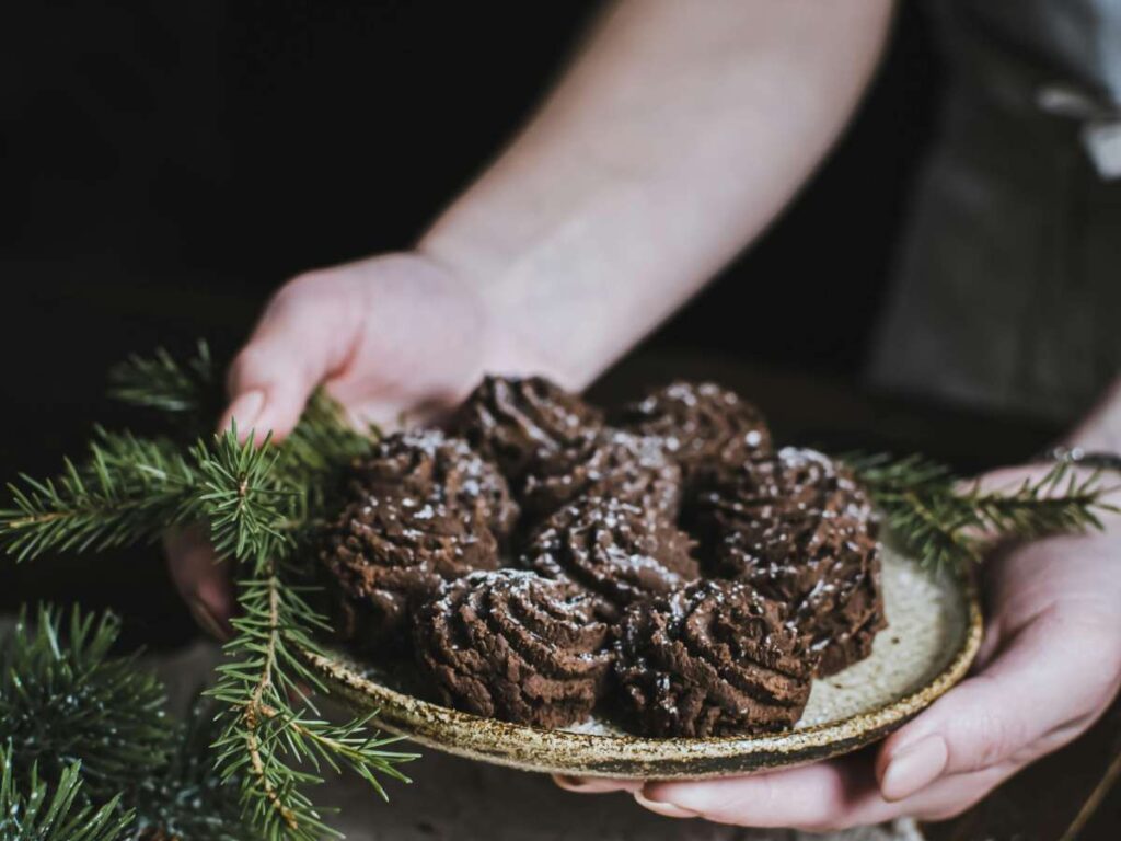 donna che tiene in mano un piatto pieno di biscotti al cioccolato e intorno dei rametti di pino