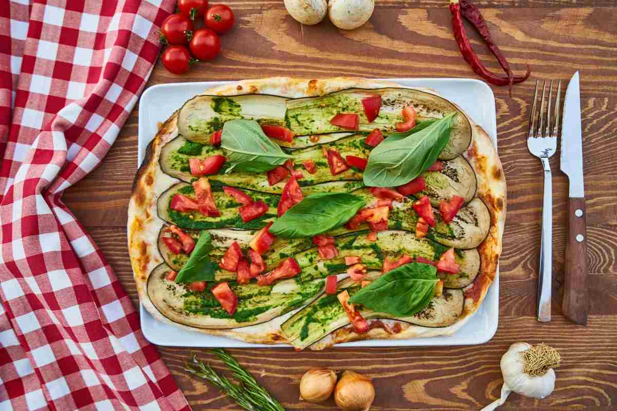 pizza con sopra zucchine a fette pomodorini e foglie di basilico