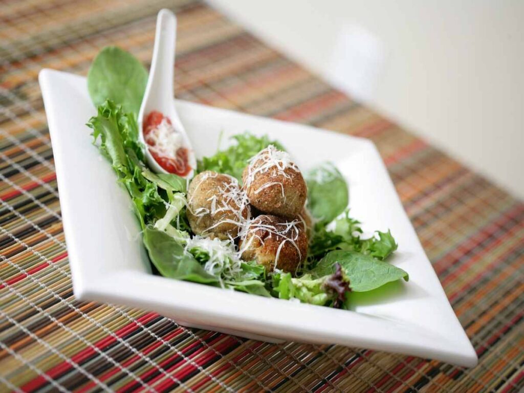 polpette dentro un piatto con insalata e un cucchiaio con salsa di pomodoro